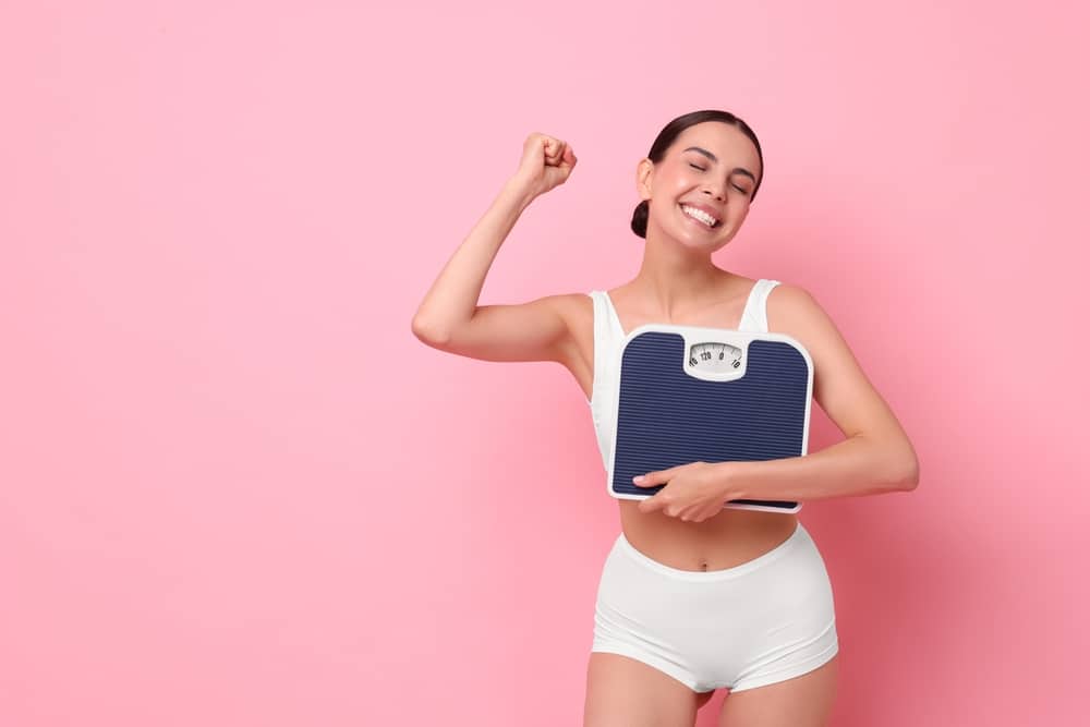 Happy woman holding scale and raising her first in victory from achieving her weight loss goal